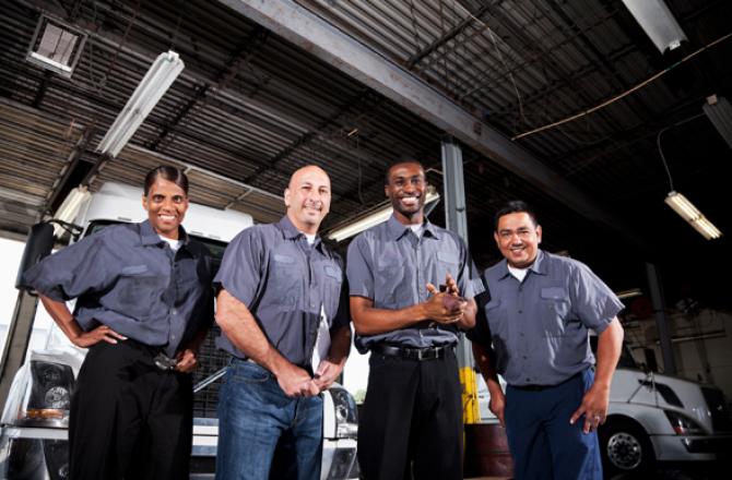 Smiling truck and coach technicians in front of a row of large trucks.