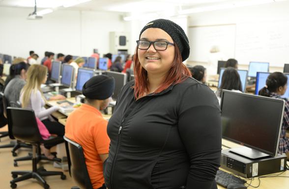 Office Administration student smiling in front of lab computers at Mohawk College