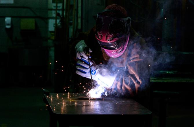 A person in full protective gear welding a piece of metal.