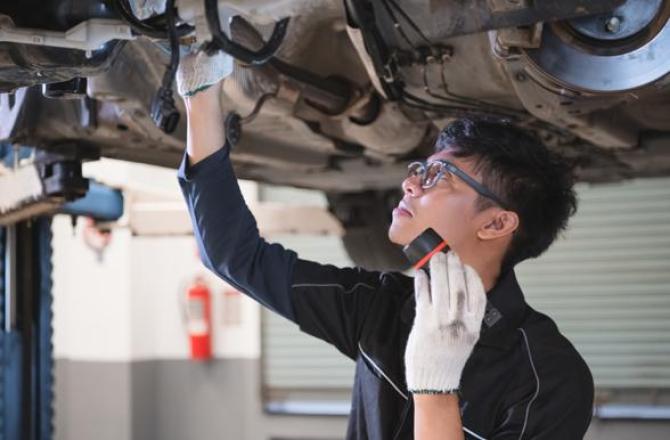 Student using a flashlight to view the underside of a vehicle on a hoist.