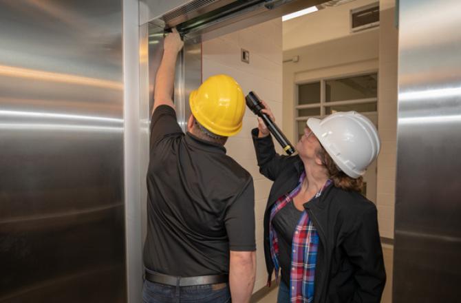 Two technicians inspecting an elevator door in Mohawk College's elevating devices lab.