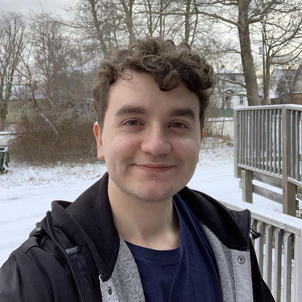 Daniel Amaral - young white man with curly hair standing outside with snow in the background. 