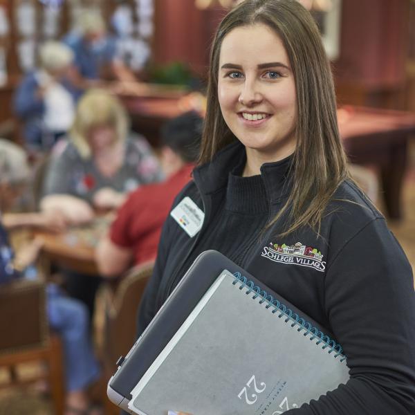Woman with binder smiles in front of long-term care residents.