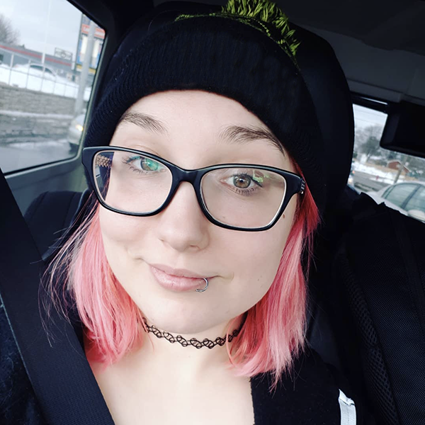 Lyndsey Wasilik smiling while sitting in her car, wearing glasses and a toque.