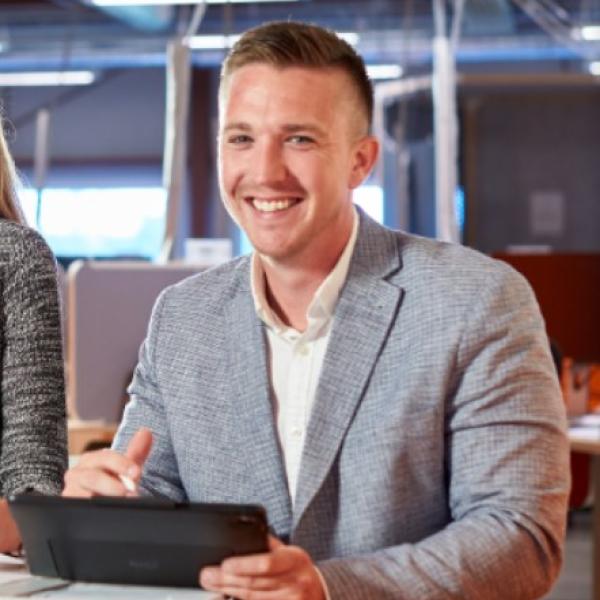 Man smiles as he reviews building schematics with co-worker off-screen.