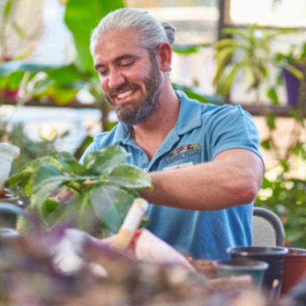Man smiles as he prunes plants with long-term care residents.