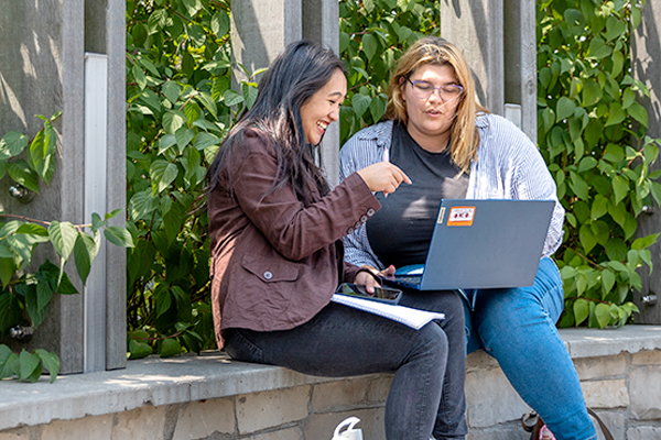 Two students sitting outside and discussing a project.